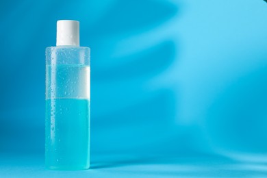 Photo of Wet bottle of micellar water on light blue background, space for text