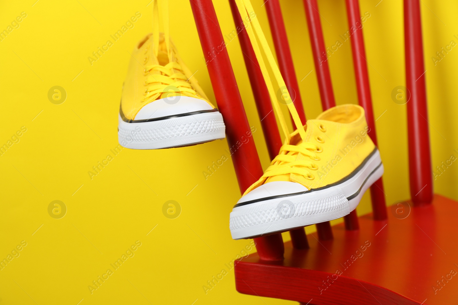 Photo of Pair of sneakers hanging on chair near yellow wall