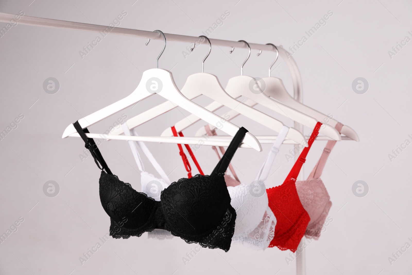 Photo of Hangers with beautiful lace bras on rack against grey background. Stylish underwear