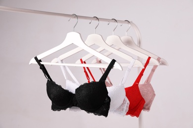 Hangers with beautiful lace bras on rack against grey background. Stylish underwear