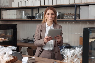 Photo of Happy business owner with tablet at cashier desk in bakery shop