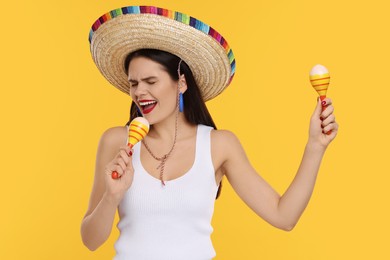 Photo of Young woman in Mexican sombrero hat with maracas on yellow background