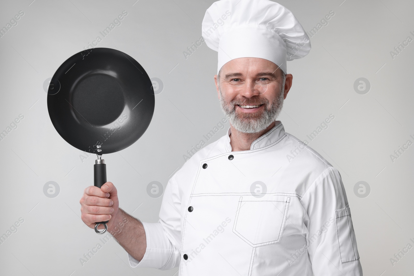 Photo of Happy chef in uniform holding wok on grey background