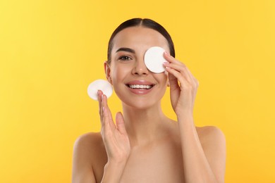 Photo of Beautiful woman removing makeup with cotton pads on yellow background