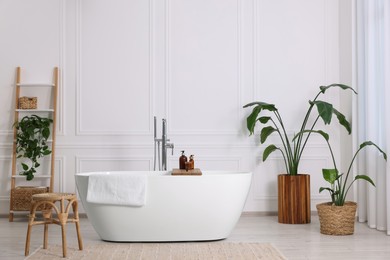 Stylish bathroom interior with beautiful tub, stool and houseplants