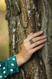 Photo of Young woman wearing beautiful silver ring with apatite gemstone near tree outdoors, closeup