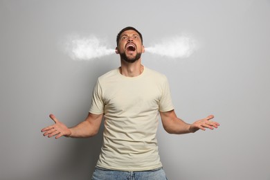 Aggressive man with steam coming out of his ears on grey background