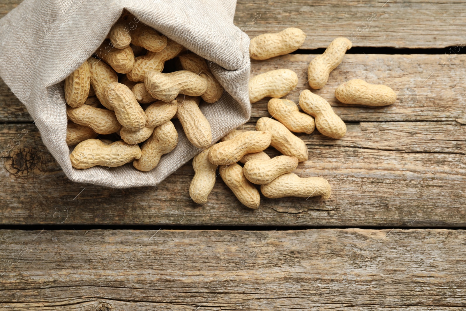 Photo of Fresh unpeeled peanuts in sack on wooden table, above view. Space for text