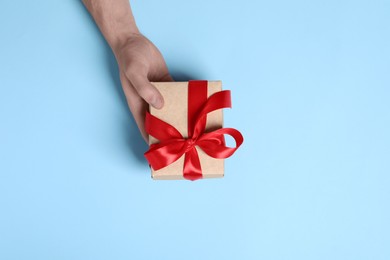 Photo of Man holding gift box with red bow on light blue background, top view