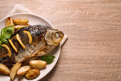 Tasty homemade roasted crucian carp with garnish on wooden table, top view and space for text. River fish