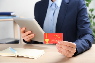 Photo of Woman with gift card and tablet at table indoors, closeup