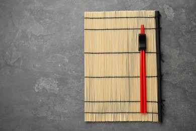 Bamboo mat with pair of red chopsticks and rest on grey table, top view. Space for text