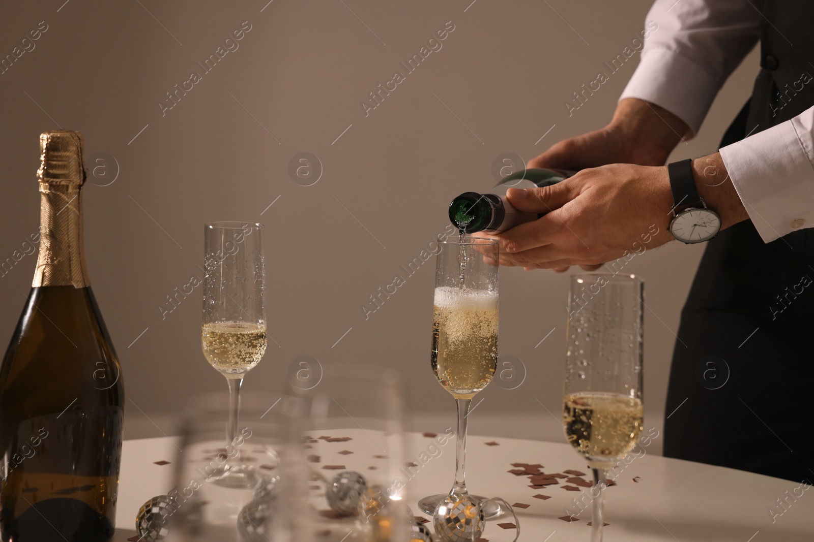 Photo of Man pouring sparkling wine into glass at table indoors, closeup. New Year celebration