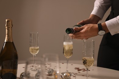 Photo of Man pouring sparkling wine into glass at table indoors, closeup. New Year celebration