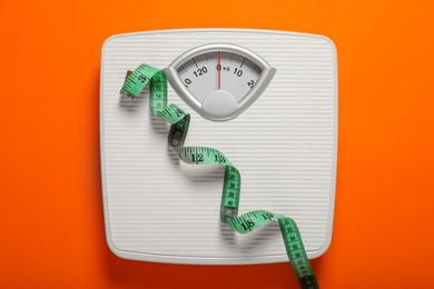 Bathroom scale and measure tape on orange background, top view