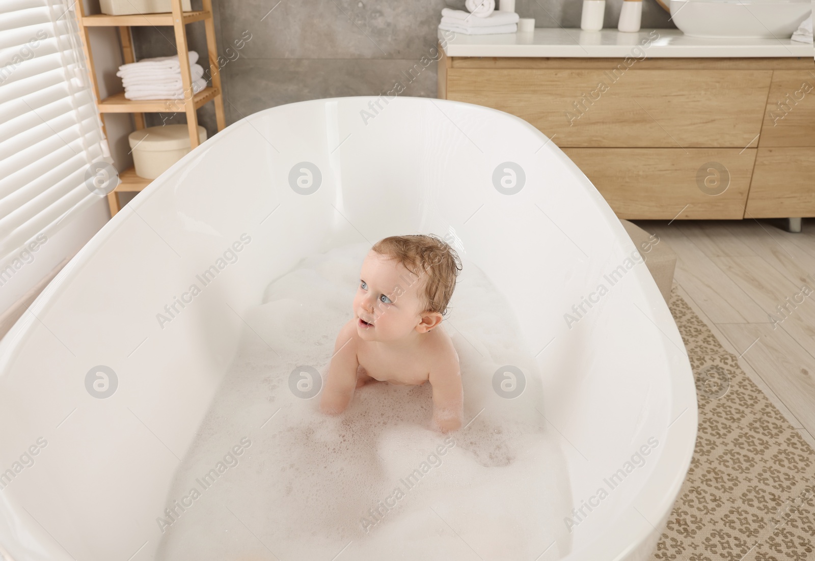 Photo of Cute little baby taking foamy bath at home