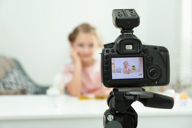 Photo of Cute little blogger with slime recording video at home, focus on camera