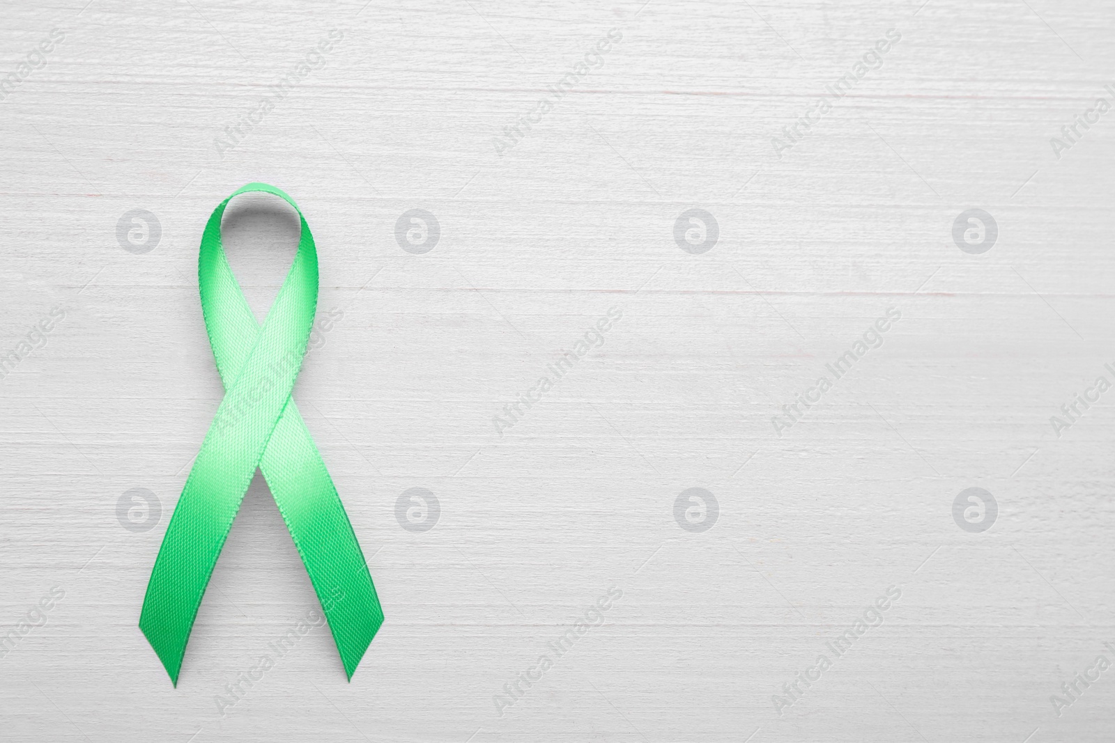 Photo of World Mental Health Day. Green ribbon on white wooden background, top view with space for text