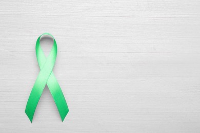 World Mental Health Day. Green ribbon on white wooden background, top view with space for text