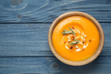 Delicious pumpkin soup in bowl on blue wooden table, top view. Space for text