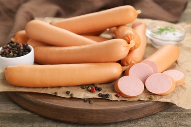 Photo of Tasty sausages and peppercorns on wooden table, closeup. Meat product
