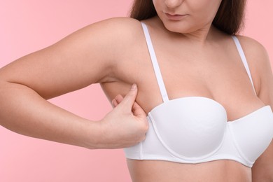 Photo of Mammology. Woman in bra doing breast self-examination on pink background, closeup