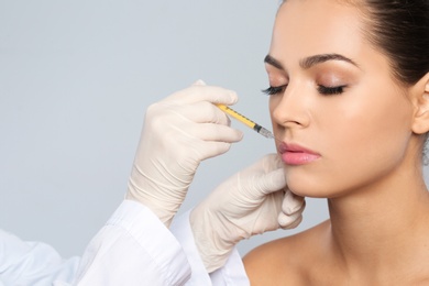 Young woman getting lips injection on grey background, space for text. Cosmetic surgery