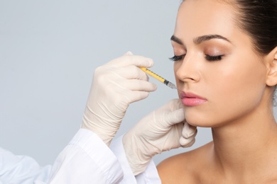 Photo of Young woman getting lips injection on grey background, space for text. Cosmetic surgery