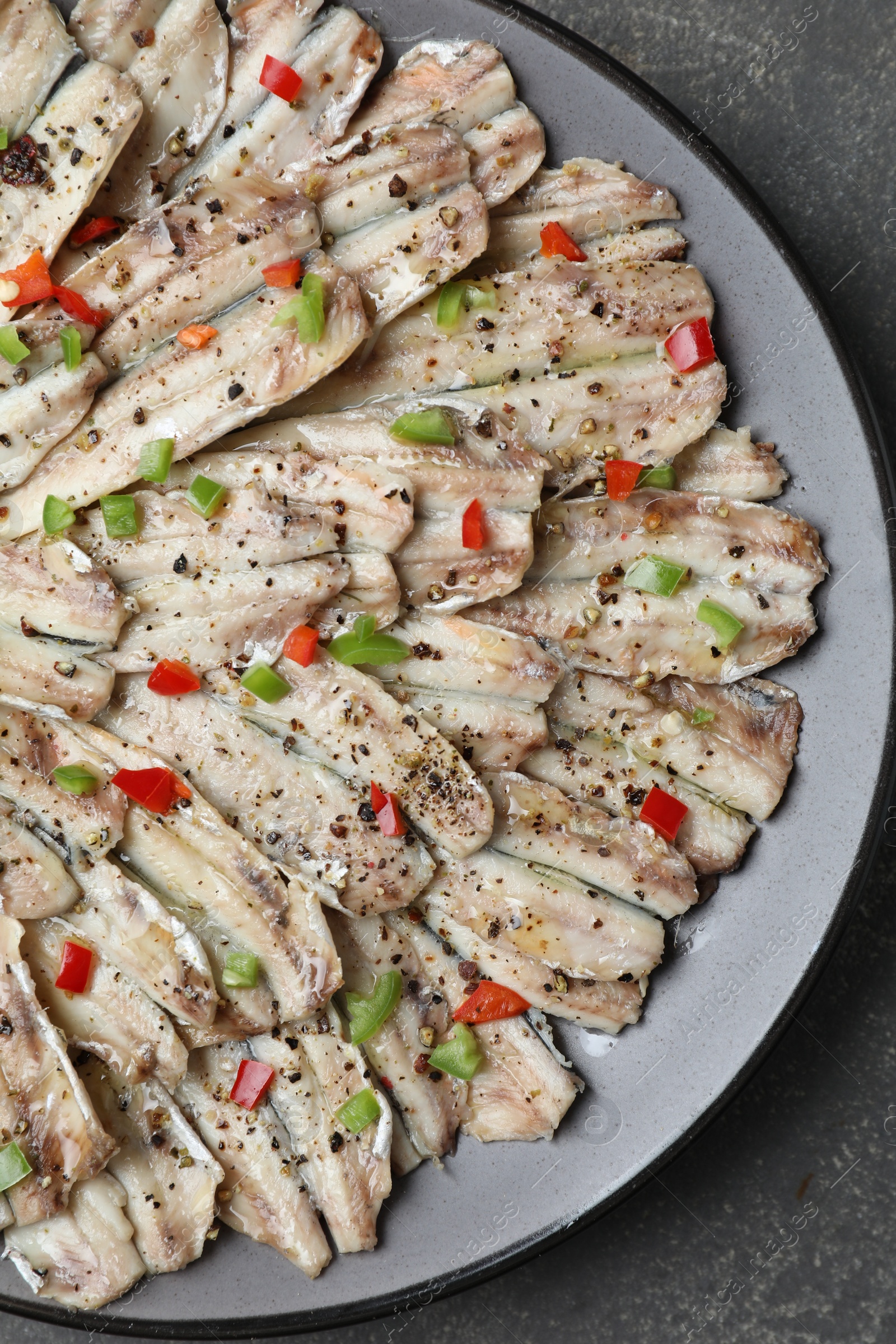 Photo of Tasty pickled anchovies with spices on grey textured table, top view