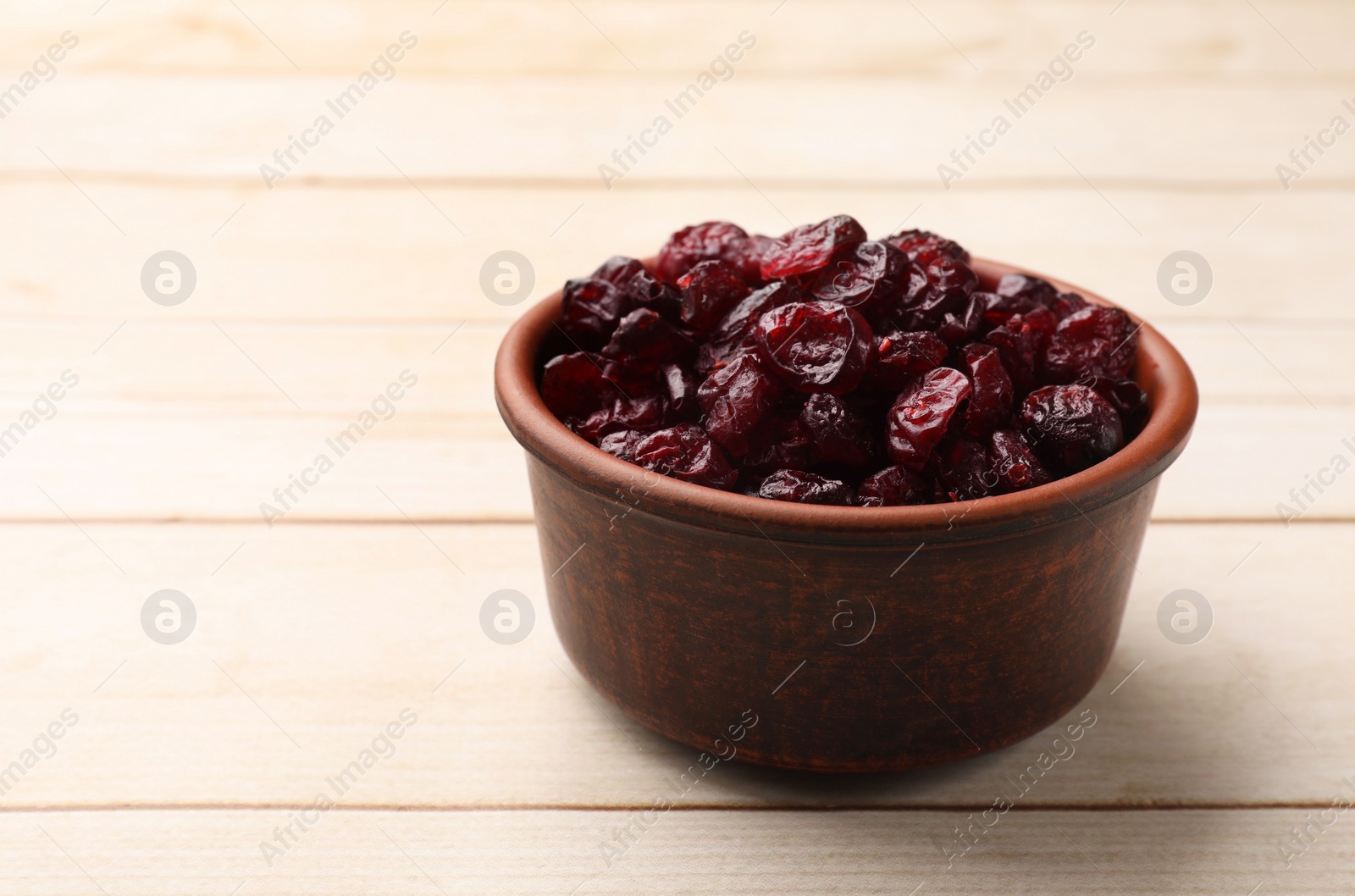 Photo of Tasty dried cranberries in bowl on light wooden table, closeup. Space for text