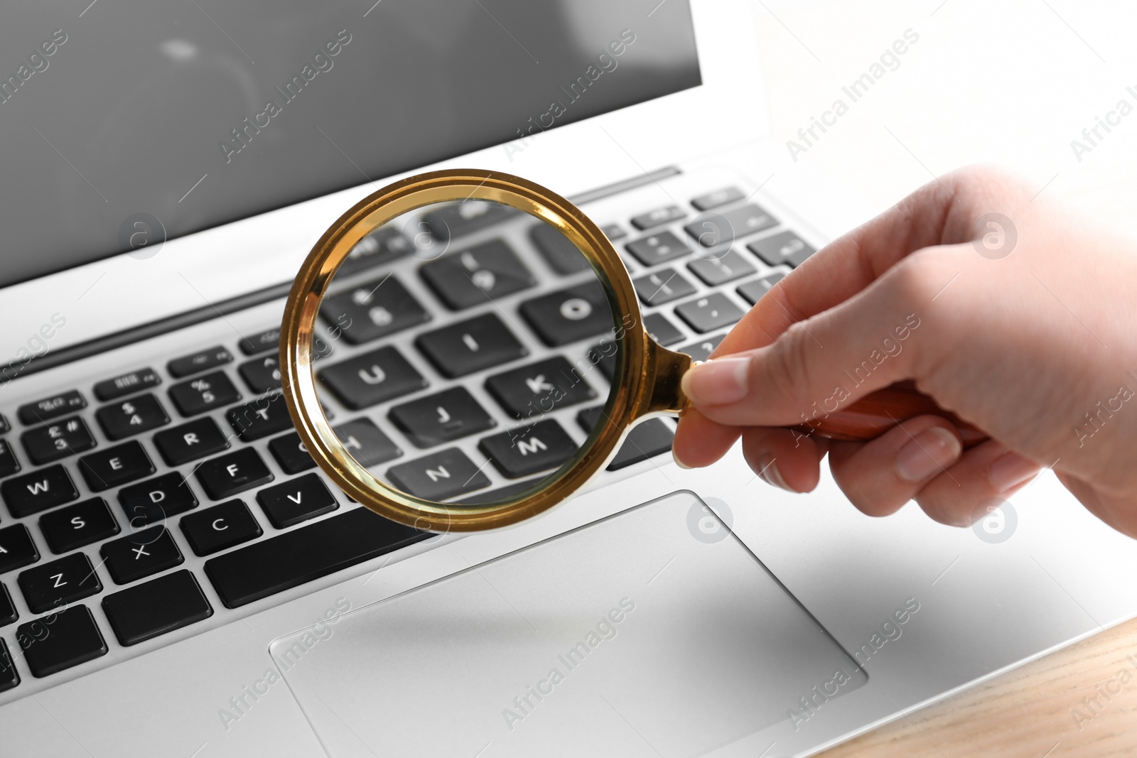 Photo of Woman looking through magnifying glass at laptop on table, closeup. Search concept