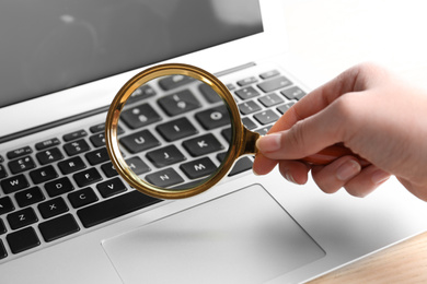 Woman looking through magnifying glass at laptop on table, closeup. Search concept