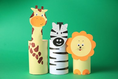 Photo of Toy giraffe, lion and zebra made from toilet paper hubs on green background. Children's handmade ideas