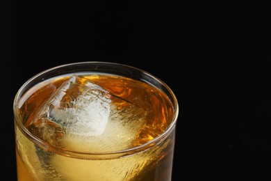 Photo of Tasty whiskey and ice in glass on black background, closeup. Space for text