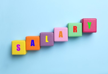 Image of Word Salary made with colorful cubes on light blue background, flat lay