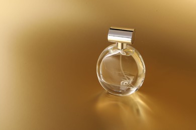 Luxury women's perfume. Sunlit glass bottle on golden background, space for text