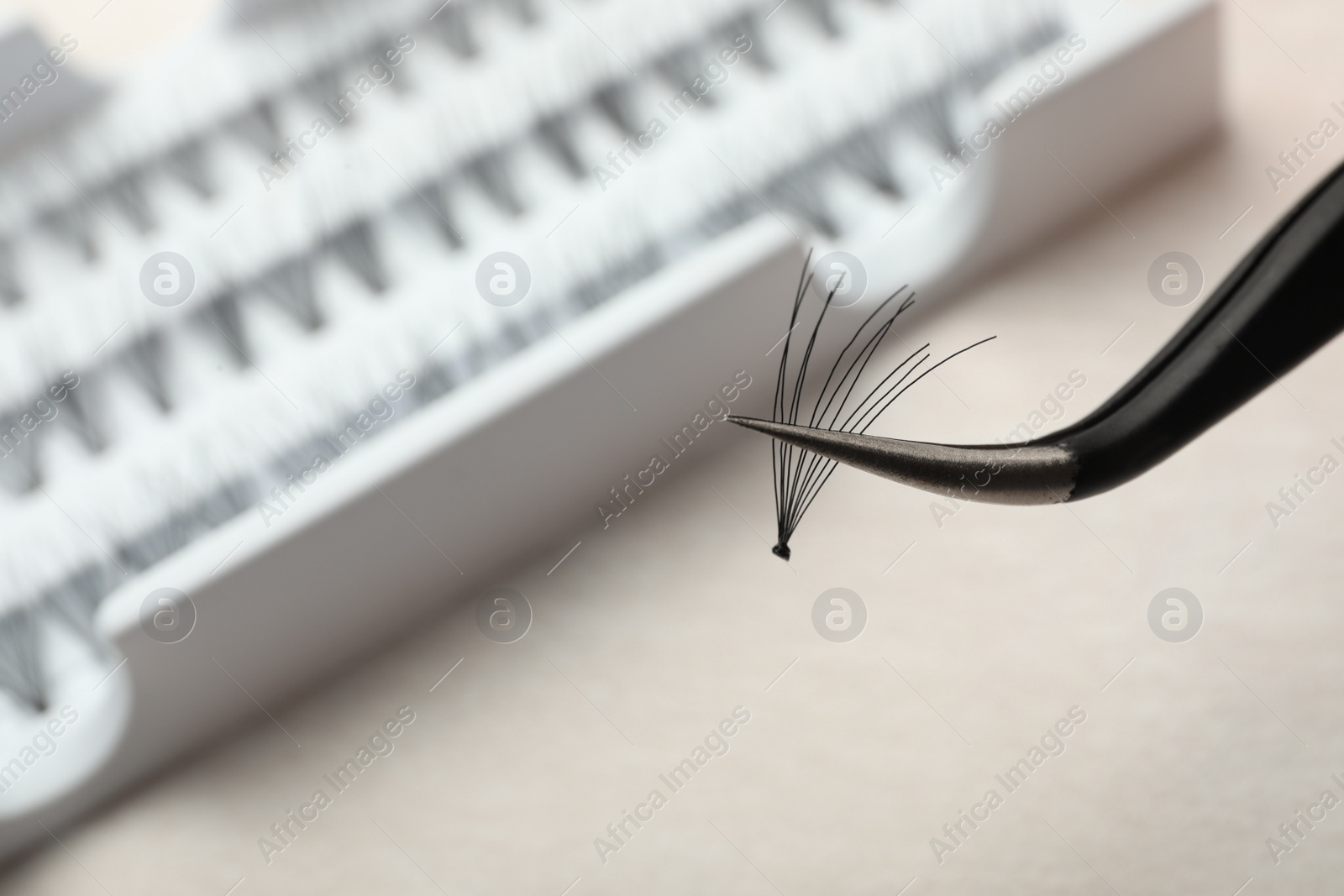Photo of Tweezers with bunch of artificial eyelashes on blurred background, closeup. Space for text