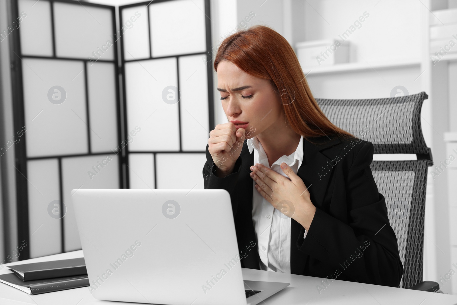 Photo of Woman coughing at table in office. Cold symptoms