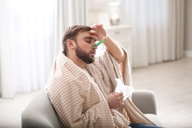 Photo of Young man with clothespin suffering from runny nose in living room