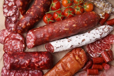 Photo of Different types of delicious sausages and tomatoes on kraft paper, flat lay