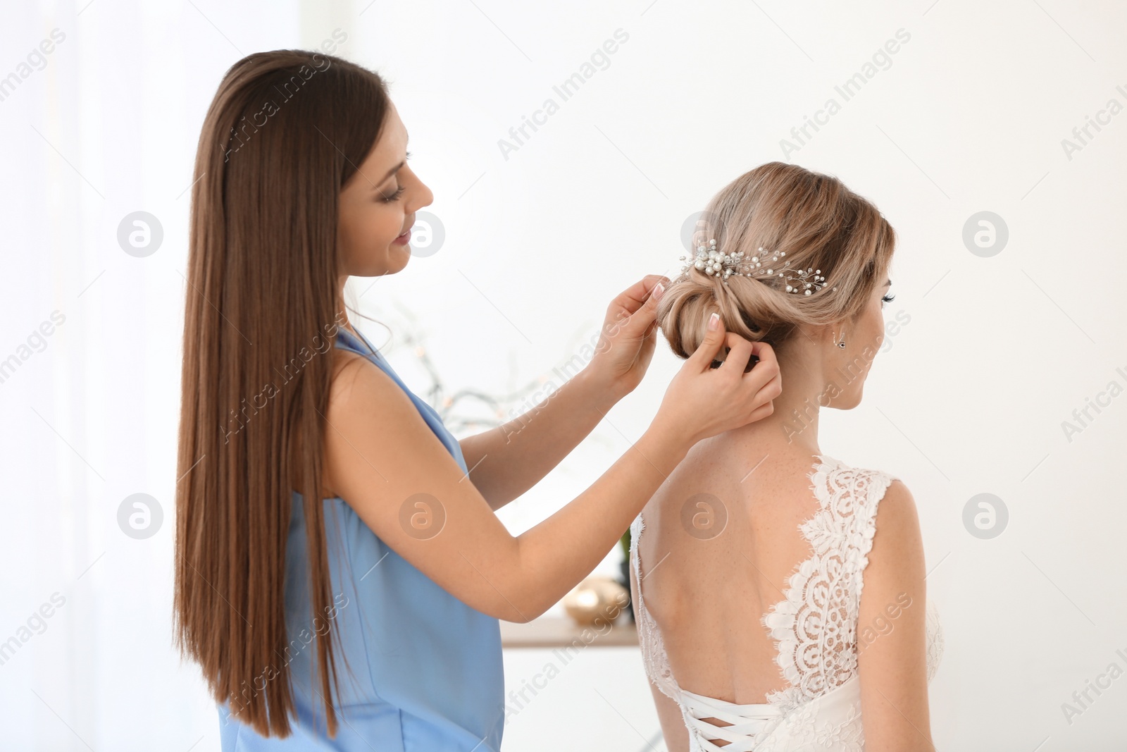 Photo of Fashion hair stylist preparing bride before her wedding indoors