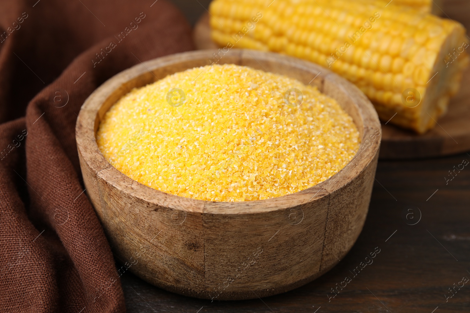 Photo of Raw cornmeal in bowl on wooden table, closeup