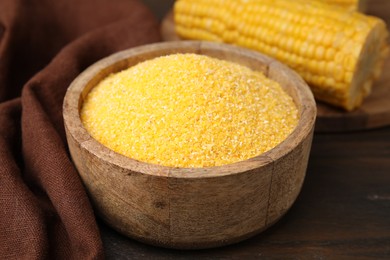 Photo of Raw cornmeal in bowl on wooden table, closeup