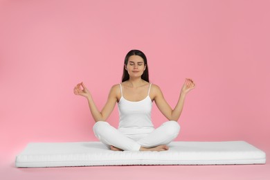 Photo of Young woman meditating on soft mattress against pink background