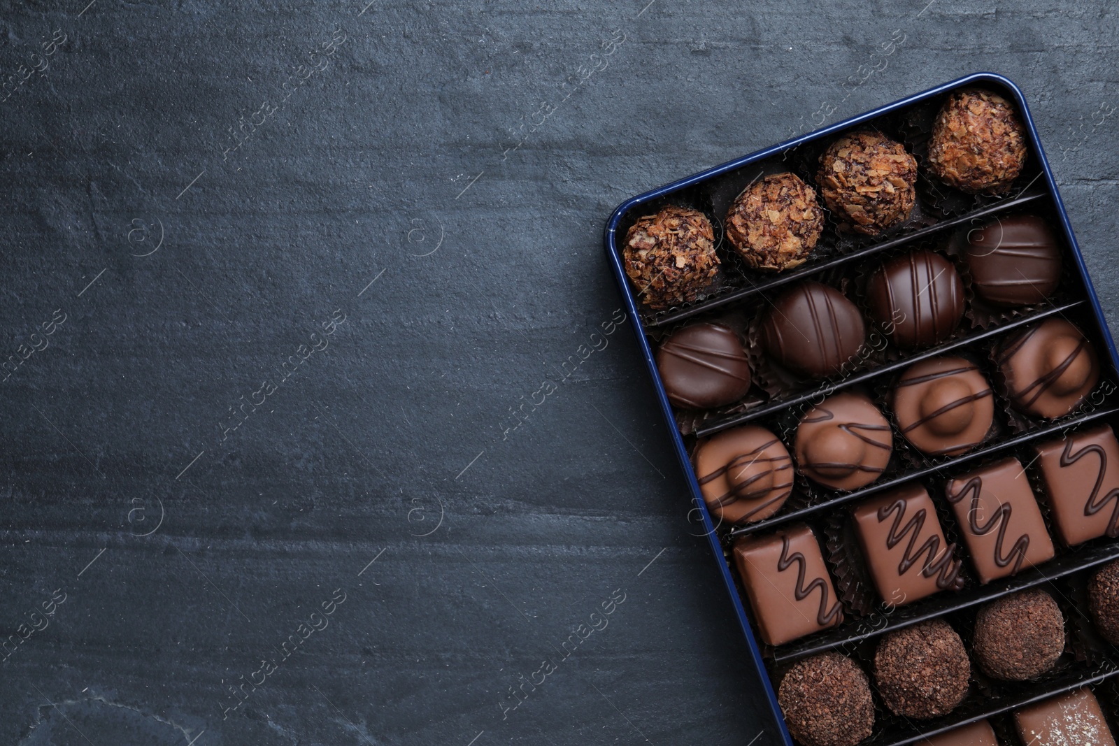 Photo of Box with delicious chocolate candies on black table, top view. Space for text