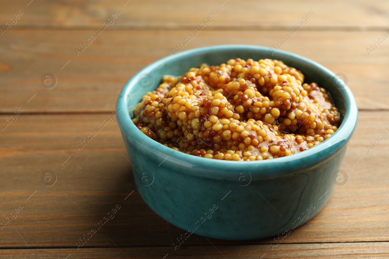 Photo of Fresh whole grain mustard in bowl on wooden table, closeup. Space for text