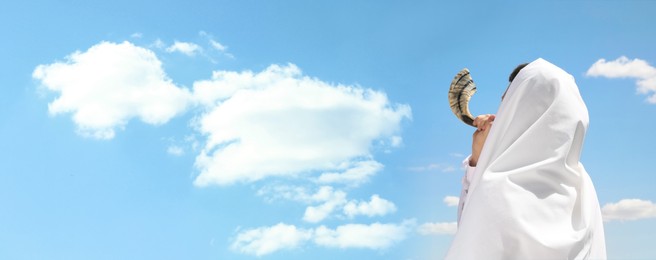 Jewish man in tallit blowing shofar outdoors, banner design. Rosh Hashanah celebration