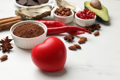 Photo of Natural aphrodisiac. Different food products and heart model on white marble table, closeup