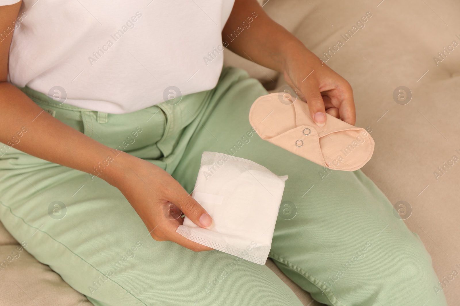 Photo of Young woman with reusable and disposable menstrual pads on sofa, closeup