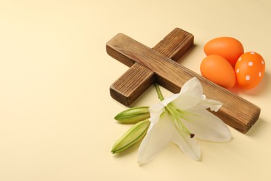 Wooden cross, painted Easter eggs and lily flowers on pale yellow background, space for text